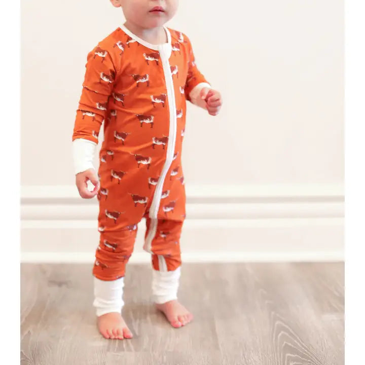 Baby wearing an orange longhorn onesie with white accents on a light wooden floor.