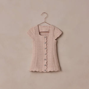 Pink textured dress on a hanger against a beige background