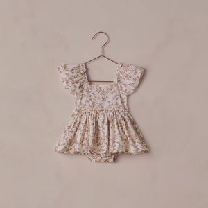 Floral baby romper on a hanger against a beige background
