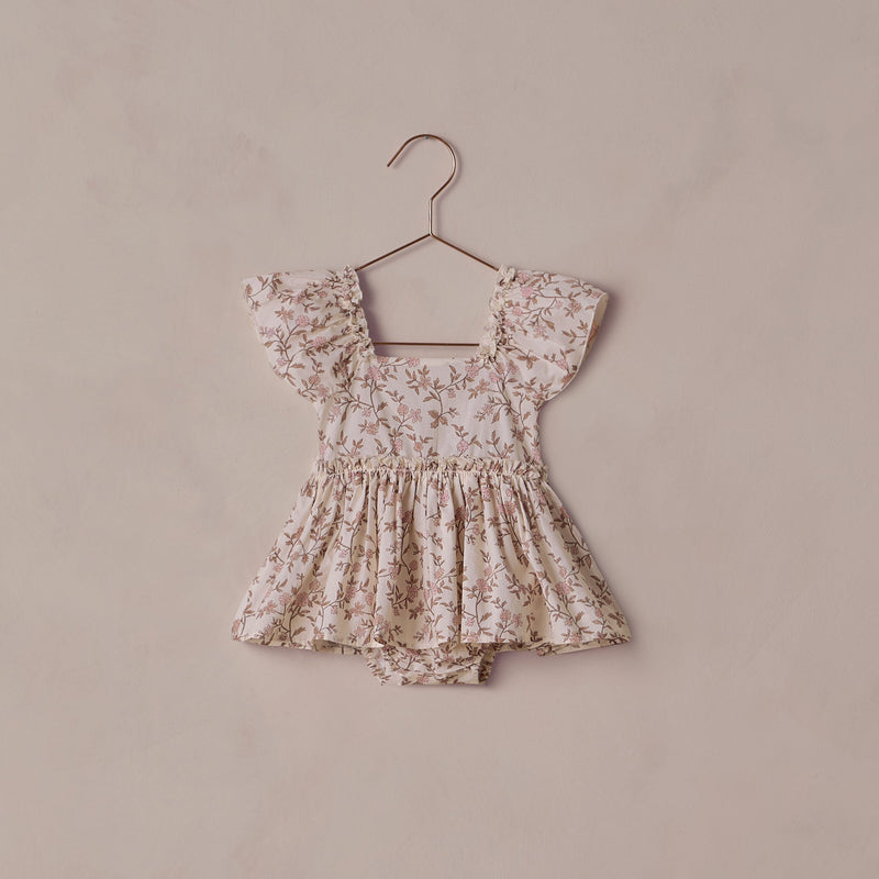 Floral baby romper on a hanger against a beige background