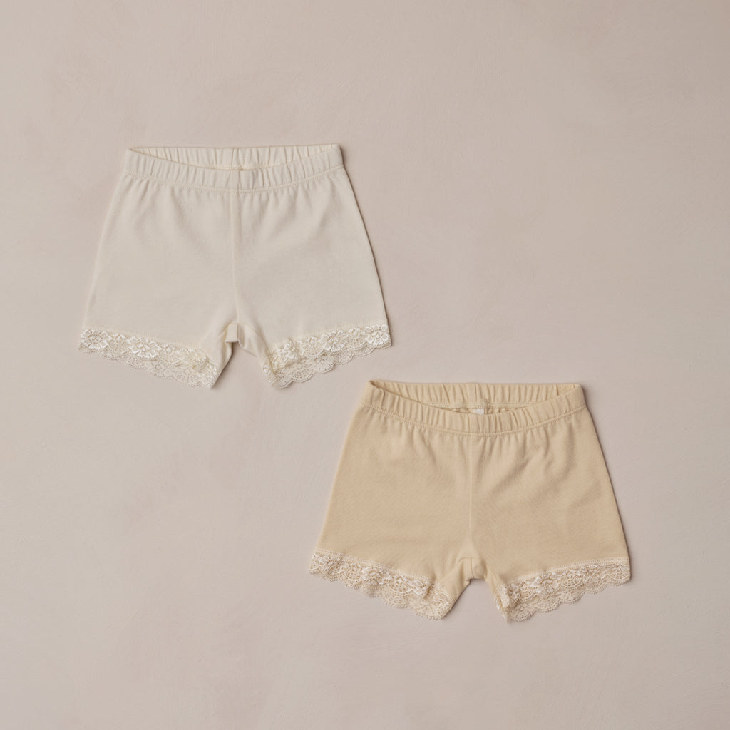 Two pairs of lace-trimmed shorts on a beige background