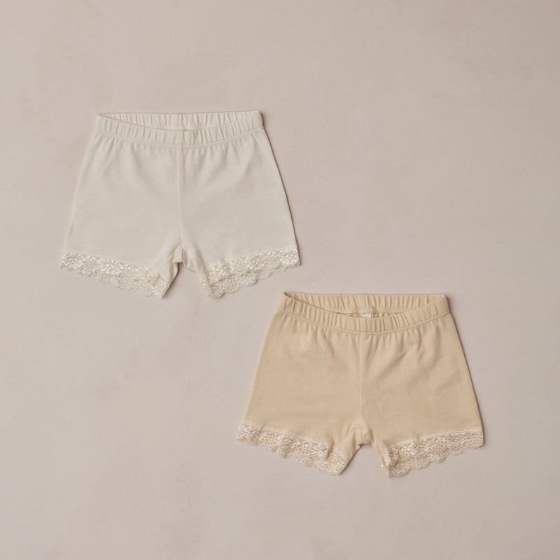 Two pairs of lace-trimmed shorts on a beige background