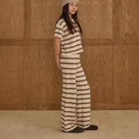 Person wearing a burgundy, beige and ivory striped pant and top against a wooden paneled wall.