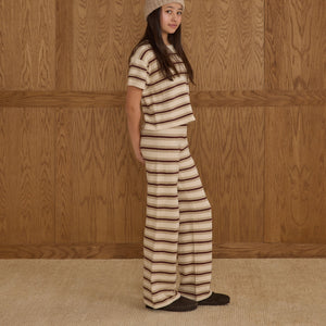 Person wearing a burgundy, beige and ivory striped pant and top against a wooden paneled wall.